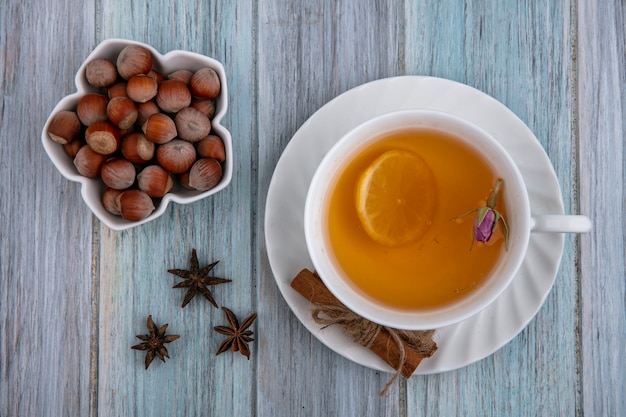 Vista superior de avellanas en un recipiente con una taza de té y una rodaja de limón con canela sobre un fondo gris