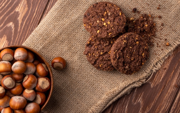 Foto gratuita vista superior de avellanas en un tazón de madera y galletas de avena en cilicio sobre madera