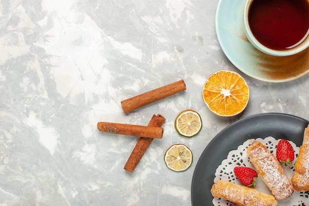 Vista superior de bagels de azúcar en polvo con fresas, canela y taza de té en el escritorio blanco