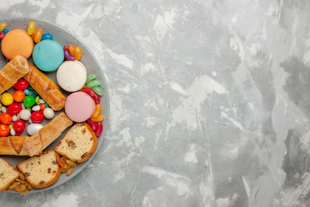 Vista superior de bagels dulces con rebanadas de pastel macarons y caramelos en superficie blanca