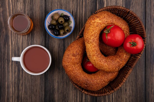 Vista superior de bagels turcos en un balde con tomates con aceitunas en un recipiente con té y miel sobre un fondo de madera