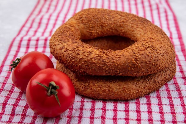 Vista superior de bagels turcos tradicionales suaves crujientes con tomates frescos sobre un paño rojo a cuadros sobre un fondo blanco.