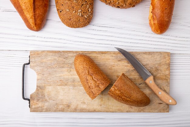 Vista superior de baguette cortado por la mitad con un cuchillo en la tabla de cortar sobre fondo de madera