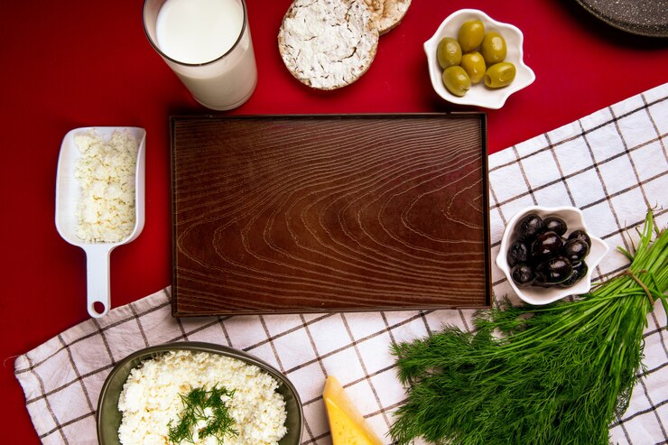 Foto gratuito vista superior de una bandeja de madera vacía y queso cottage en un tazón con aceitunas en escabeche eneldo y pasteles de arroz sobre tela escocesa en rojo