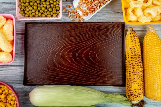Vista superior de la bandeja vacía con guisantes verdes semillas de maíz cereales de maíz pop y mazorcas de maíz en superficie de madera