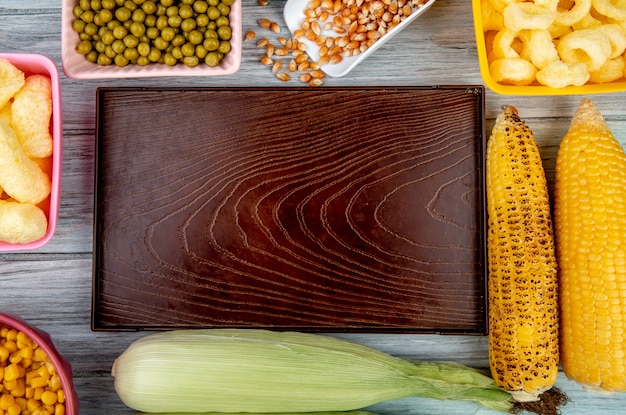 Vista superior de la bandeja vacía con guisantes verdes semillas de maíz cereales de maíz pop y mazorcas de maíz en superficie de madera