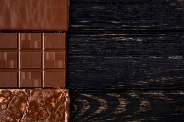 Vista superior de la barra de chocolate sobre fondo rústico oscuro con espacio de copia