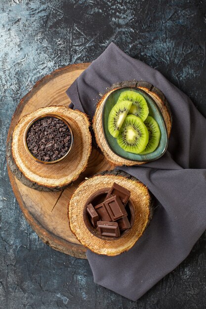 Vista superior de barras de chocolate con kiwis frescos en rodajas en la superficie de color gris oscuro pastel color desayuno azúcar postre de frutas