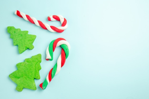 Vista superior de bastones de caramelo y galletas en forma de árbol en superficie azul