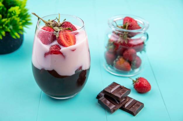 Vista superior de batido con chocolate y fresas en un vaso con barra de chocolate sobre superficie azul