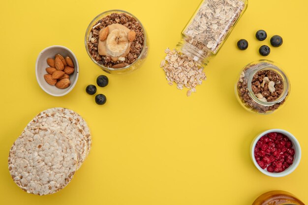 Vista superior del batido con mantequilla de maní de plátano, leche de almendras y nueces en vaso con pan de avena, endrino de grosella roja sobre fondo amarillo