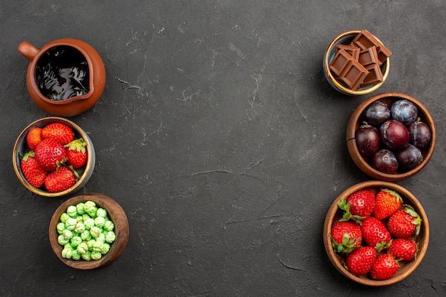 Vista superior bayas y dulces salsa de chocolate fresas chocolate verde caramelos y bayas en tazones marrones sobre la mesa