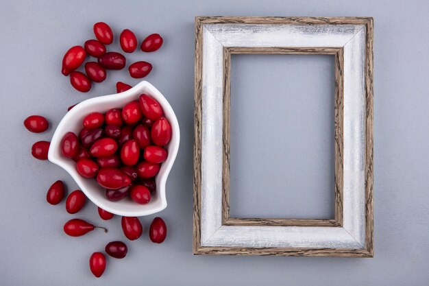 Foto gratuita vista superior de bayas frescas de cornel rojo en un recipiente blanco sobre un fondo gris con espacio de copia