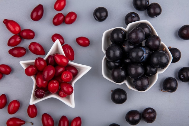 Foto gratuita vista superior de bayas frescas de cornel rojo en un recipiente en forma de estrella con uvas negras sobre un fondo gris