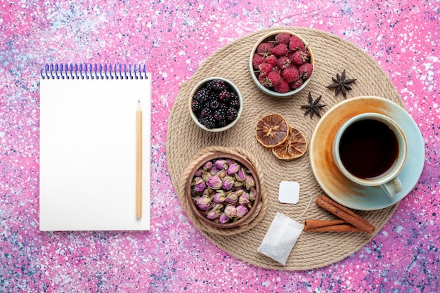 Vista superior de bayas frescas frambuesas y moras con taza de té y canela sobre fondo rosa.