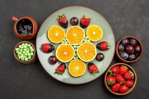 Vista superior de bayas lejanas y plato de chocolate de naranja picada y fresas cubiertas de chocolate junto a los tazones con dulces bayas nd salsa de chocolate