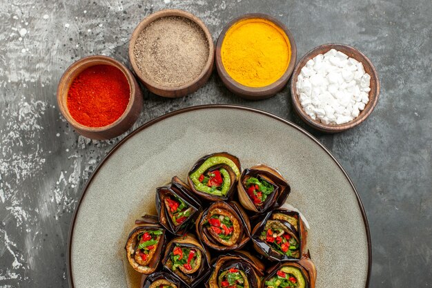 Vista superior de berenjena rellena rollos de cúrcuma en polvo de pimiento picante en tazones pequeños sobre superficie gris