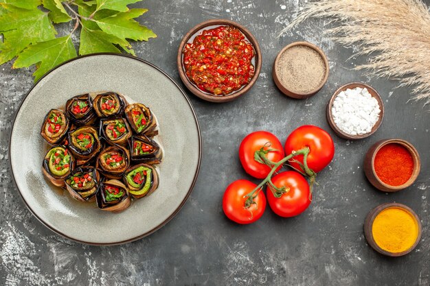 Vista superior de berenjena rellena rollos de especias en tazones pequeños sal pimienta pimiento rojo cúrcuma tomates adjika sobre fondo gris