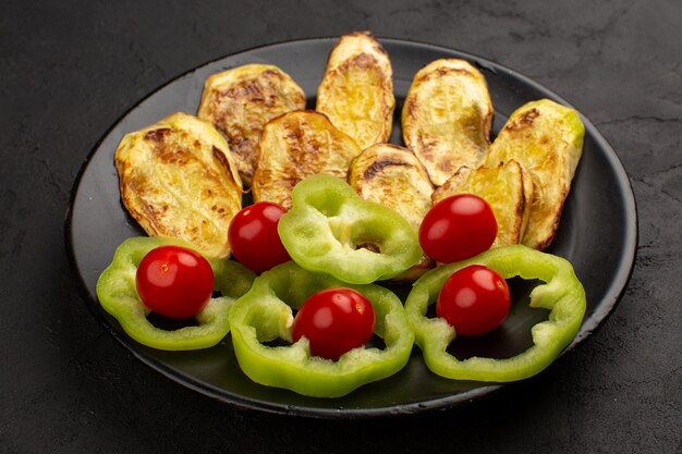 vista superior berenjenas cocidas junto con pimiento verde en rodajas y tomates enteros dentro de un plato negro en la oscuridad