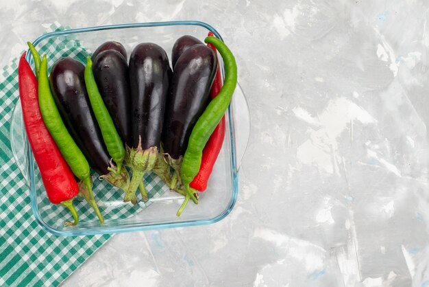 Vista superior berenjenas crudas con pimientos de colores en la comida vegetal de escritorio brillante