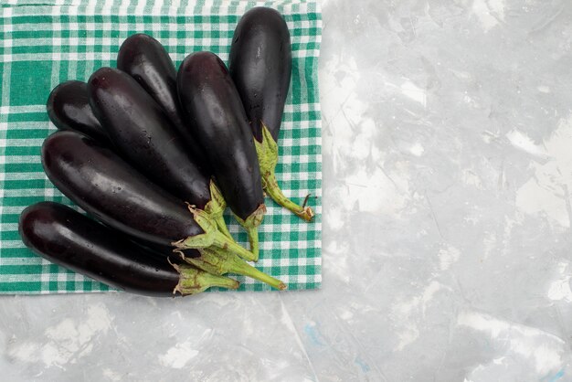 Vista superior berenjenas negras frescas maduras frescas en el brillante escritorio comida vegetal plato de comida cruda