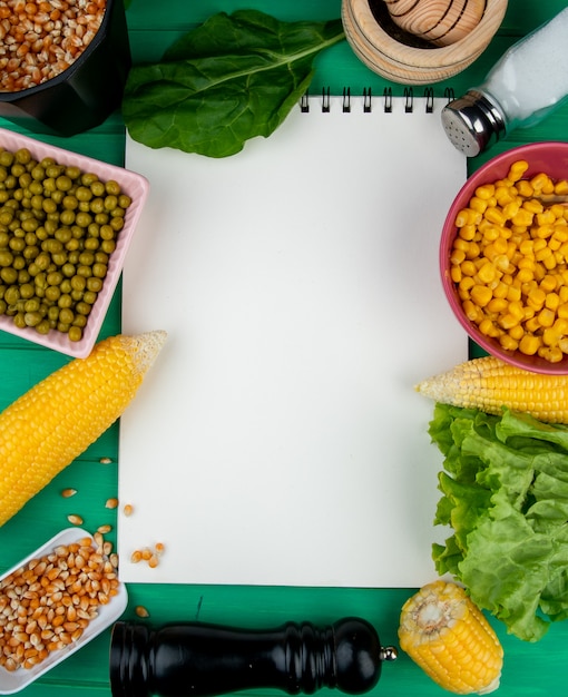 Vista superior del bloc de notas con callos semillas de maíz guisantes verdes espinacas lechuga y sal alrededor en verde con espacio de copia