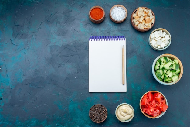 Vista superior del bloc de notas y verduras con condimentos en el color de la comida de aperitivos de comida vegetal de fondo azul oscuro