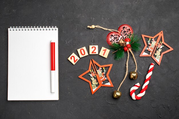 Vista superior del bloque de madera adornos de Navidad marcador rojo de caramelo de Navidad en el bloc de notas sobre fondo oscuro aislado