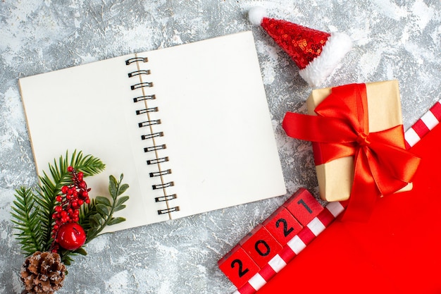 Vista superior de bloques de madera de regalo de navidad cuaderno pequeño sombrero de santa rama de árbol de navidad en mesa blanca gris