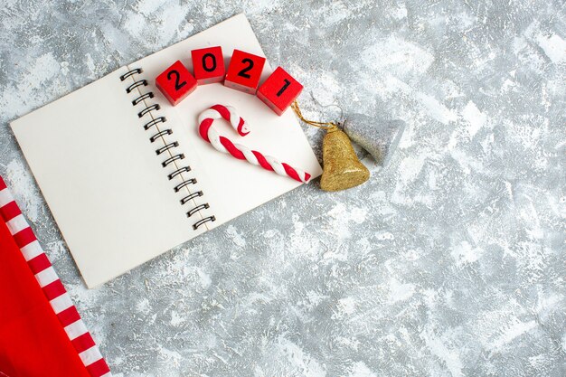 Vista superior de bloques de madera roja dulces de Navidad en el cuaderno, campanas de Navidad en la mesa blanca gris con lugar libre