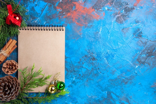 Vista superior de bolas de árbol de Navidad en un cuaderno ramas de pino piña en superficie azul espacio libre