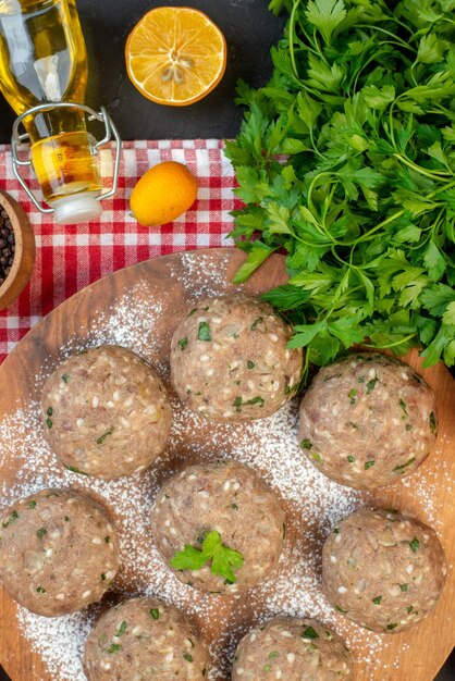 Foto gratuita vista superior de bolas de carne sin cocer con verde en un plato marrón y una botella de aceite caída de limón verde fresco sobre una toalla roja pelada sobre fondo negro