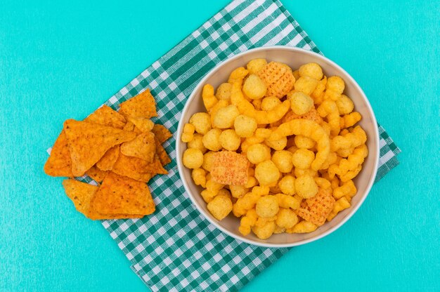 Vista superior de bolas de maíz en un tazón con chips en servilleta y horizontal azul
