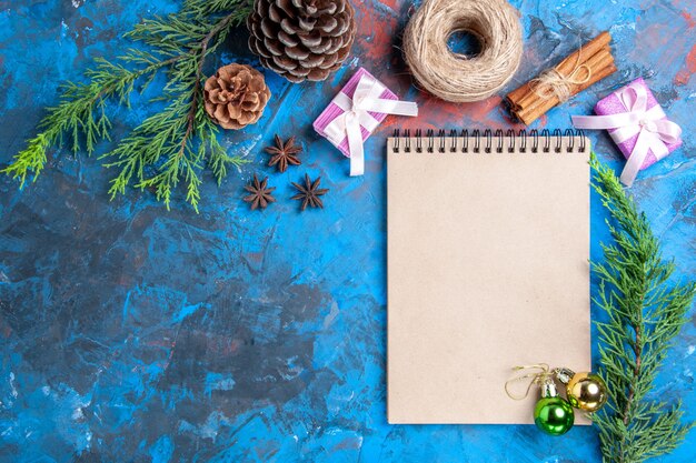 Vista superior de bolas de navidad en un cuaderno ramas de pino ramas de canela anís rodajas de limón secas en la superficie azul lugar libre