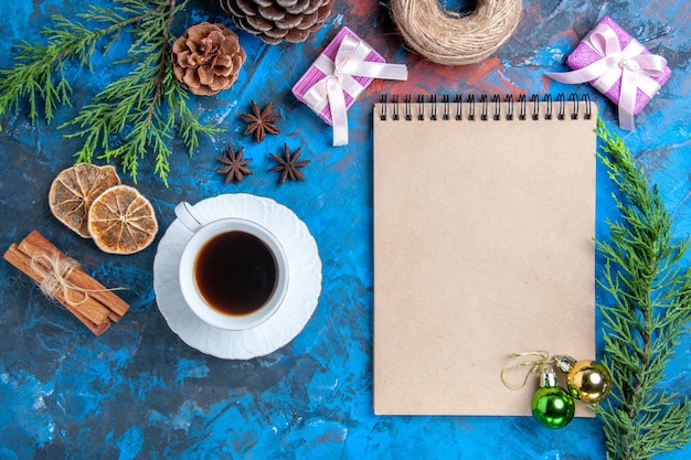 Vista superior de bolas de Navidad en un cuaderno ramas de pino ramas de canela anís rodajas de limón seco una taza de té sobre superficie azul