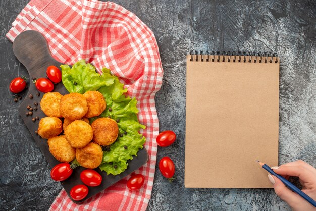 Vista superior de bolas de queso frito en lápiz de tabla de cortar en el bloc de notas de mano femenina