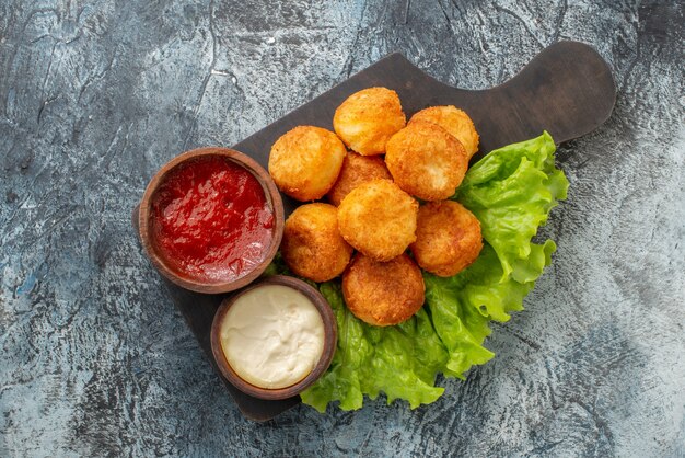 Vista superior de bolas de queso frito salsas en tazones pequeños sobre tabla de cortar vista superior bolas de queso frito tazones de salsa de lechuga en una tabla de cortar