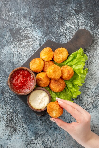 Vista superior bolas de queso frito tazones de salsa de lechuga en tabla de cortar bola de queso en mano femenina en la mesa