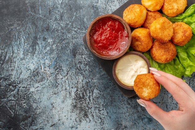 Vista superior bolas de queso frito tazones de salsa de lechuga en tabla de cortar bola de queso en mano de mujer en la mesa