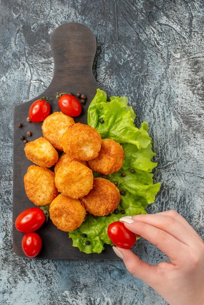 Vista superior de bolas de queso frito tomates cherry lechuga en tabla de cortar tomate cherry en mano femenina