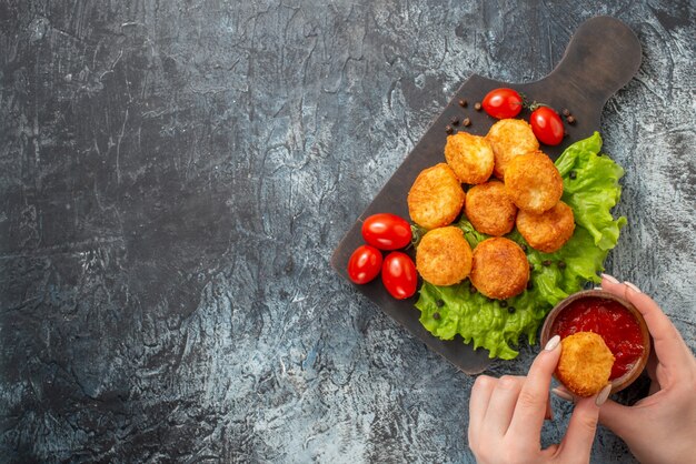 Vista superior de bolas de queso frito tomates cherry en tazón de fuente de ketchup de tabla de cortar y bola de queso en manos femeninas