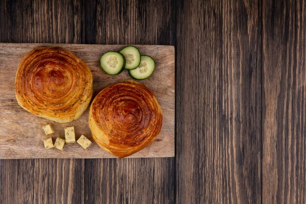 Vista superior de bollos en una tabla de cocina de madera con rodajas picadas de pepino y queso sobre un fondo de madera con espacio de copia