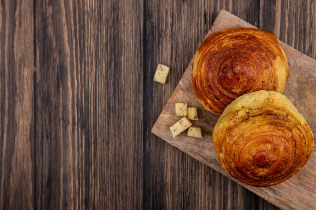 Vista superior de bollos en una tabla de cocina de madera con rodajas de queso picadas sobre un fondo de madera con espacio de copia