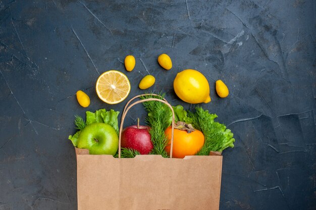 Vista superior de la bolsa de compras manzanas verdes y rojas caqui hojas de limón cumcuats sobre fondo oscuro