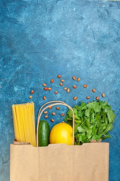 Foto gratuita vista superior bolsa de compras de papel limón espaguetis pepino cilantro frijoles en mesa azul