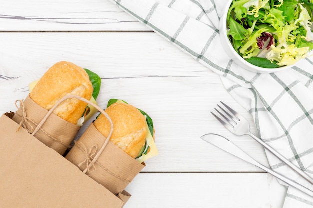 Vista superior de la bolsa de papel con dos sándwiches dentro y ensalada