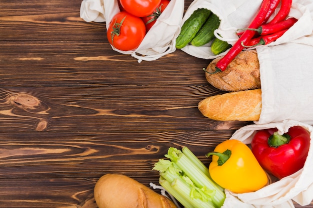 Vista superior de bolsas reutilizables en superficie de madera con frutas y verduras.