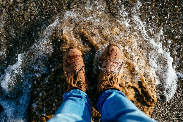 Vista superior de las botas de los hombres marrones en la playa de piedra, de la onda. Fondo de piedras de mar.