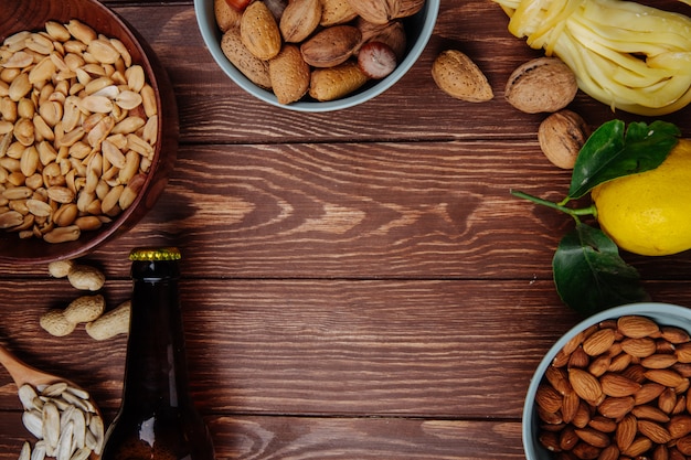 Vista superior de una botella de cerveza con una mezcla de bocadillos salados, maní, queso de almendras con limón sobre madera rústica con espacio de copia