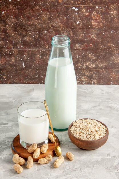 Vista superior de la botella de vidrio y la taza llena de leche en la bandeja de madera y frutos secos cuchara avena en una olla marrón sobre una mesa blanca sobre fondo marrón